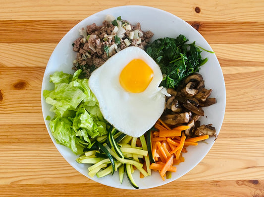 Colorful Korean bibimbap bowl topped with fresh microgreens and fried egg